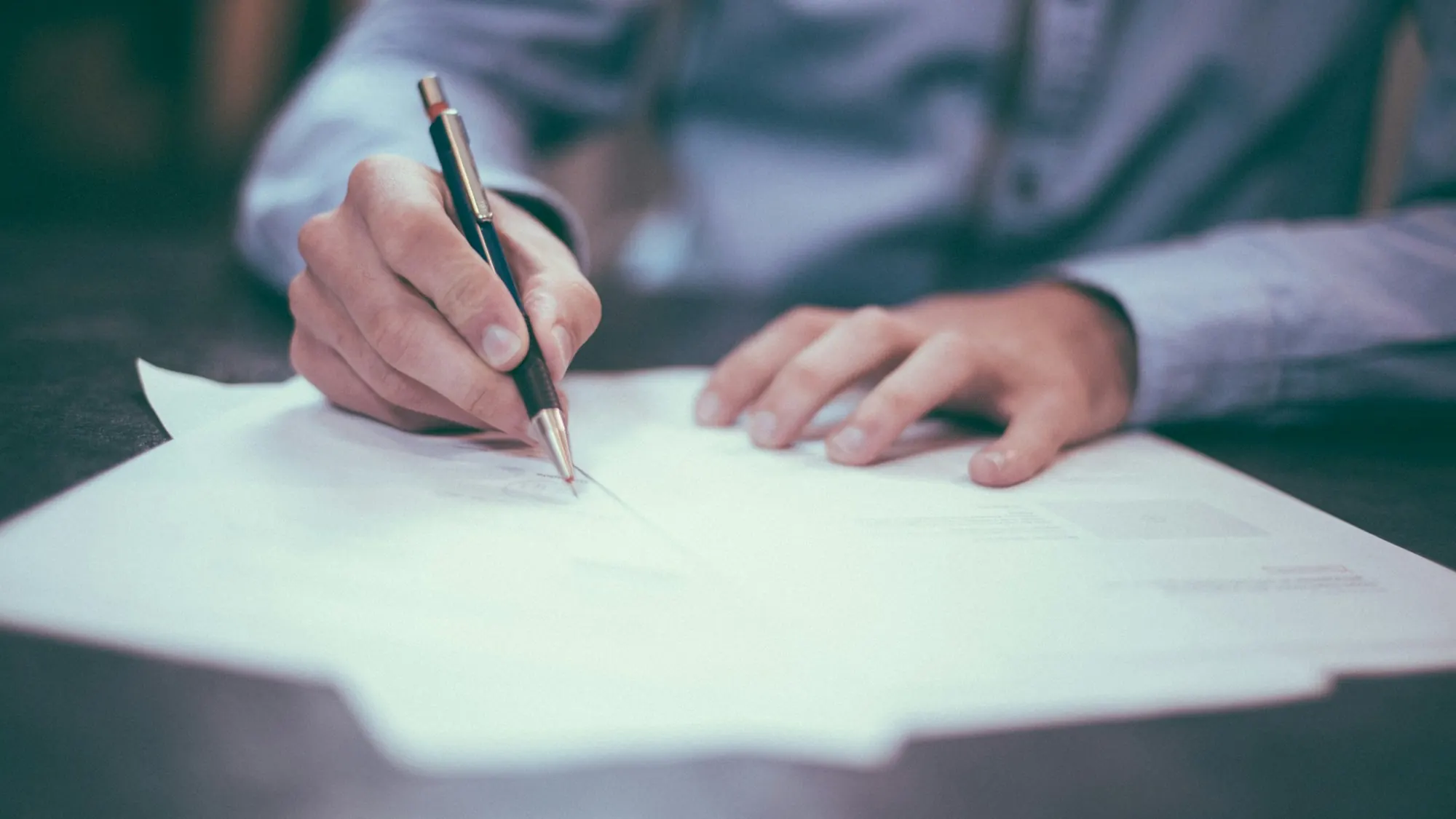 Persona escribiendo a mano sobre un documento en la mesa